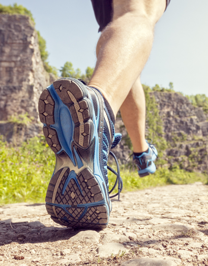 A person jogging on a scenic trail, showcasing proper footwear for running and hiking, emphasizing podiatric health